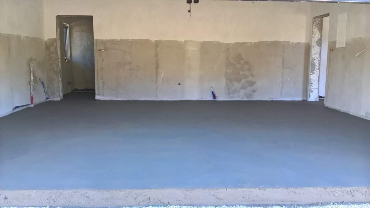 Świeżo wylana, gładka posadzka jastrychowa w surowym wnętrzu z widocznymi śladami prac wykończeniowych na ścianach i narzędziami w tle.