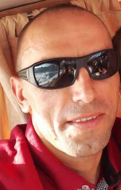 Mężczyzna w okularach przeciwsłonecznych, w których odbija się krajobraz z górą i transportem, prawdopodobnie podczas podróży.