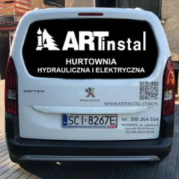 Oklejony tył białego samochodu Peugeot Rifter z reklamą firmy ARTinstal, hurtowni hydraulicznej i elektrycznej, widoczny adres strony internetowej, numer telefonu i kod QR.