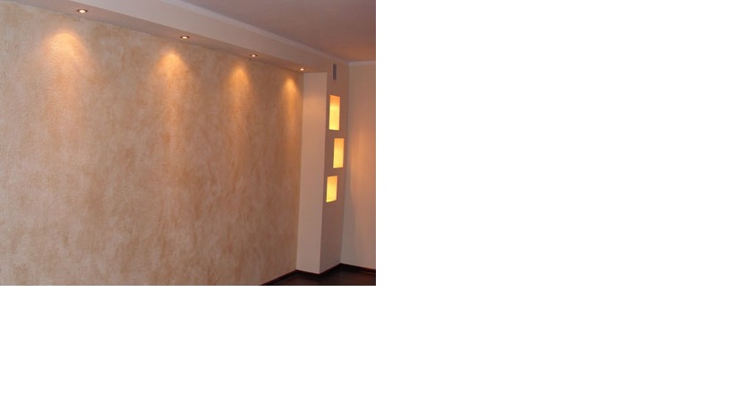 Ściana z dekoracyjną fakturą w odcieniach beżu i brązu, oświetlona punktowymi lampami sufitowymi i pionową wnęką z trzema podświetlonymi półkami.