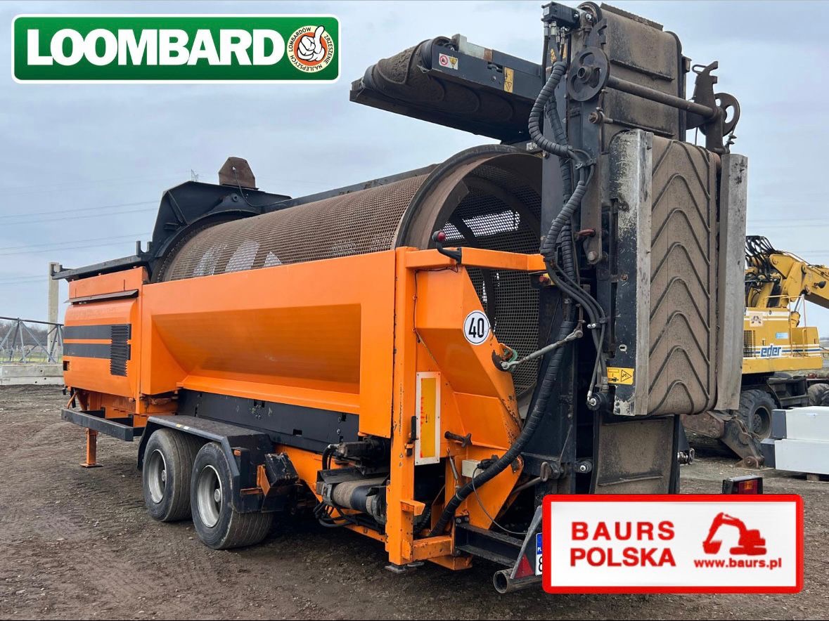 Pomarańczowa przesiewarka mobilna, widok z tyłu. Na drugim planie częściowo widoczna koparka. Urządzenie na podwoziu kołowym z elementami siatki i taśmociągu.