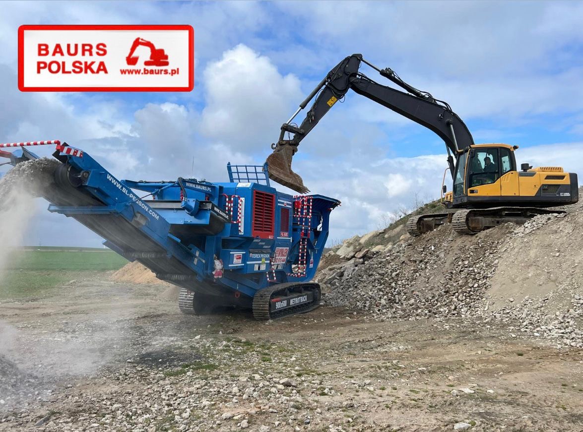 Żółta koparka Hyundai EC220D podnosi urobek na niebieski przesiewacz mobilny Terex Finlay 883+ z logo Baur's Polska na tle pochmurnego nieba.