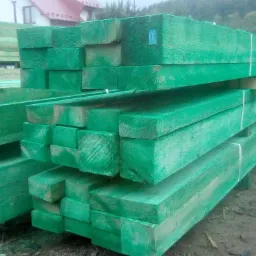 Stosy impregnowanych na zielono belek drewnianych o przekroju kwadratowym, ułożone na zewnątrz, widoczne ślady po impregnacji ciśnieniowej.