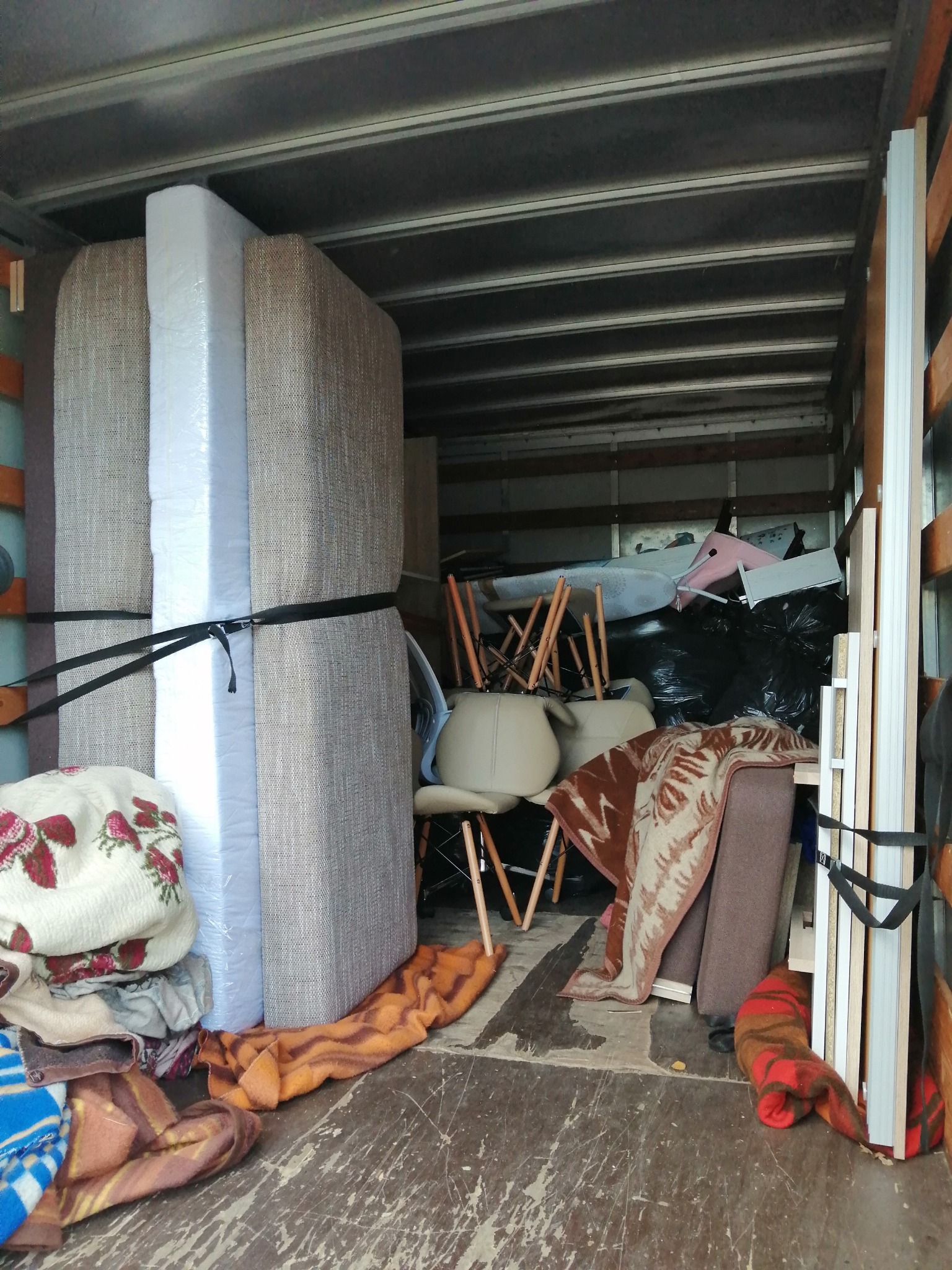 Wnętrze przestrzeni ładunkowej wypełnione meblami, krzesłami i workami, zabezpieczonymi pasami, przygotowanymi do przewozu.