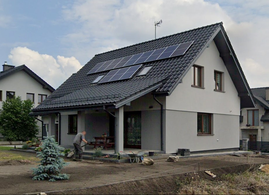 Nowoczesny dom jednorodzinny z panelami słonecznymi na dachu, widoczny fragment ogrodu z pracującą osobą. Dom zlokalizowany w Czeladzi, ul. Asnyka.