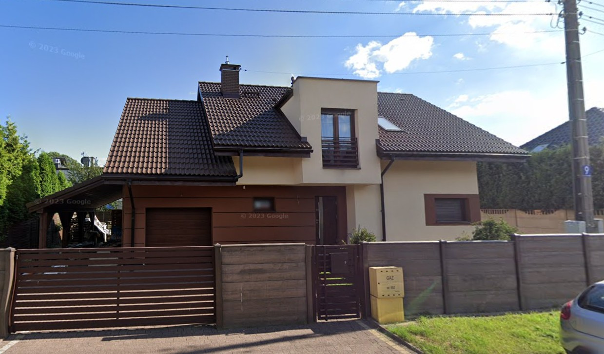 Dwukondygnacyjny dom jednorodzinny z brązowym dachem i elementami w kolorze beżowym, z garażem po lewej stronie, widziany z poziomu ulicy w Siemianowicach Śląskich.