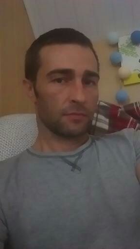 Portret mężczyzny w szarej koszulce na tle ściany z dekoracjami. Ujęcie z bliska, oświetlenie naturalne.