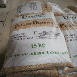Stos worków z pelletem drzewnym marki Darton, każdy o wadze 15 kg, z widocznymi parametrami jakości i danymi kontaktowymi producenta, ułożonych na betonowej posadzce magazynu.