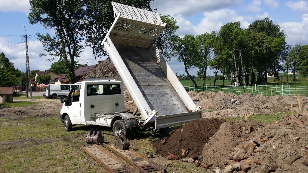 Wyładowany gruz z wywrotki na placu budowy w słoneczny dzień. Widoczne drzewa w tle.