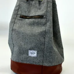 Szary, tekstylny plecak-worek z brązową, skórzaną podstawą, zamykany na sznurek, z kieszenią na zamek. Widoczne logo 'BenWild'.