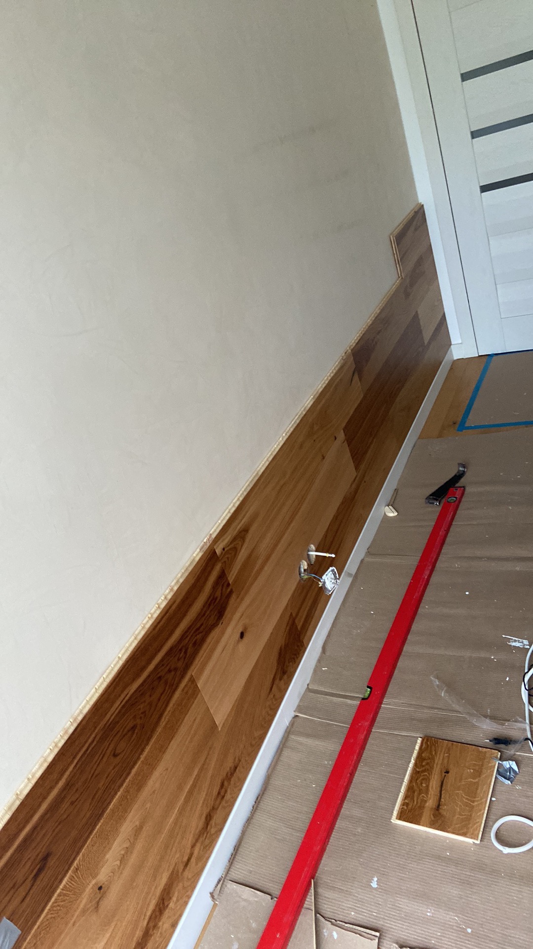 Montaż drewnianej okładziny ściennej w Pruszczu Gdańskim, widoczny poziomica, fragment podłogi zabezpieczony kartonem, ściana pomalowana na jasny kolor.