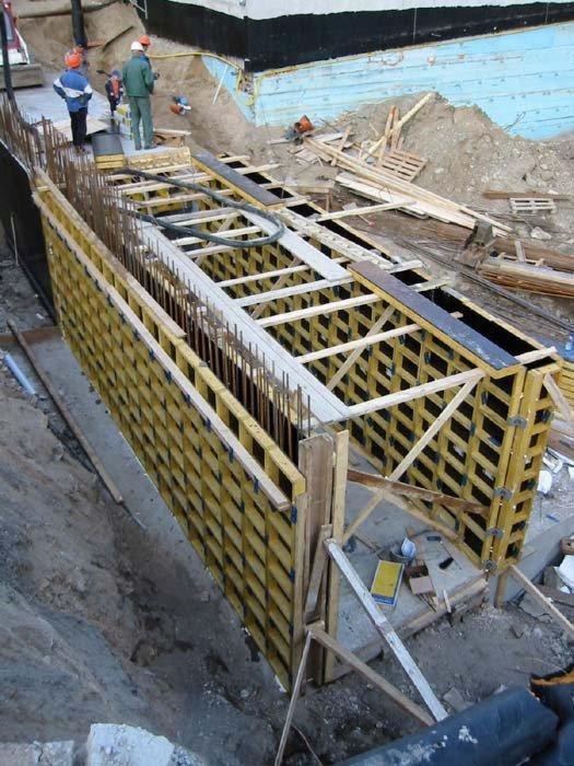 Szalunek systemowy w wykopie pod fundamenty, widoczne zbrojenie i pracownicy w oddali, teren budowy.