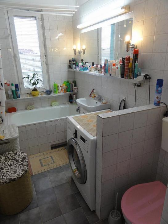 Jasna łazienka z wanną, pralką i toaletą w bloku mieszkalnym, widok na okno z roletami.