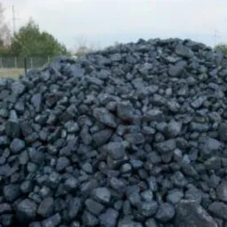 Góra węgla kostki w składzie, widoczne białe worki w tle, pochmurne niebo.