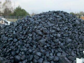 Góra węgla kostki w składzie, widoczne białe worki w tle, pochmurne niebo.