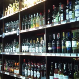 Półki w sklepie z alkoholem, wypełnione różnorodnymi butelkami wódek, win i likierów. Widoczne ceny na półkach, oświetlenie punktowe.