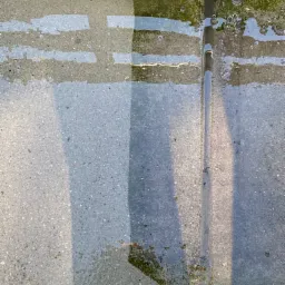 Fragment kostki brukowej, częściowo umytej, z widoczną różnicą w kolorze i czystości przed i po czyszczeniu, z wodą zbierającą się w zagłębieniach.