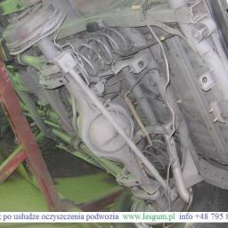 Kooperacja Polsko-Niemiecka LES-GUM Export-Import Leszek Wydrzyński - Oczyszczone podwozie Jeepa na podnośniku, widok z dołu. Elementy zawieszenia, sprężyny i układ wydechowy w szarym kolorze po zabiegu czyszczenia.