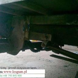 Kooperacja Polsko-Niemiecka LES-GUM Export-Import Leszek Wydrzyński - Zardzewiała rama pojazdu przed czyszczeniem, widoczne elementy zawieszenia i koło. Niska jakość zdjęcia, słabe oświetlenie. Widoczny adres strony internetowej.