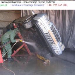 Kooperacja Polsko-Niemiecka LES-GUM Export-Import Leszek Wydrzyński - Mycie podwozia srebrnego Mercedesa, umieszczonego na specjalnym stelażu, przez pracownika w kombinezonie ochronnym. Woda pod ciśnieniem.