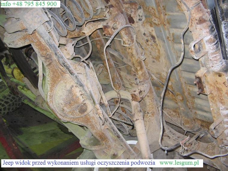 Zardzewiałe podwozie Jeepa przed czyszczeniem w Dębicy. Widoczne elementy zawieszenia i liczne ogniska korozji. Ujęcie od dołu.