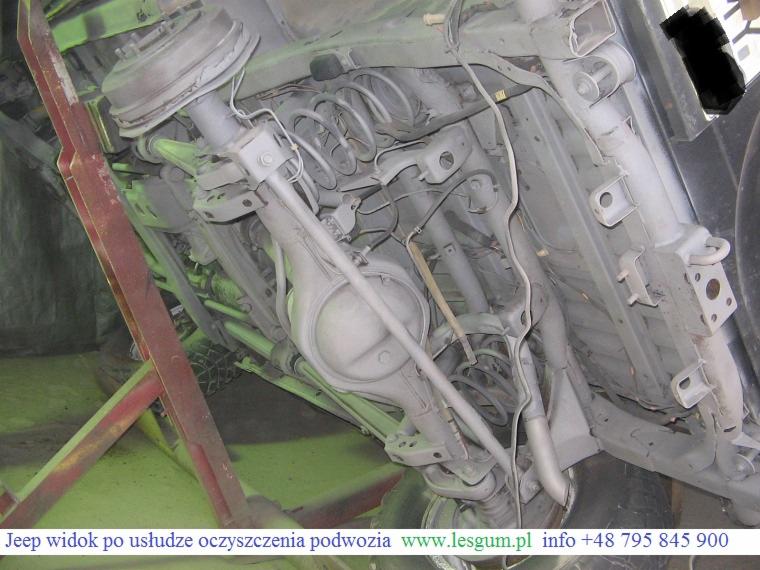 Oczyszczone podwozie Jeepa na podnośniku, widok z dołu. Elementy zawieszenia, sprężyny i układ wydechowy w szarym kolorze po zabiegu czyszczenia.
