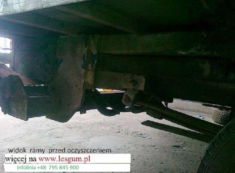 Zardzewiała rama pojazdu przed czyszczeniem, widoczne elementy zawieszenia i koło. Niska jakość zdjęcia, słabe oświetlenie. Widoczny adres strony internetowej.