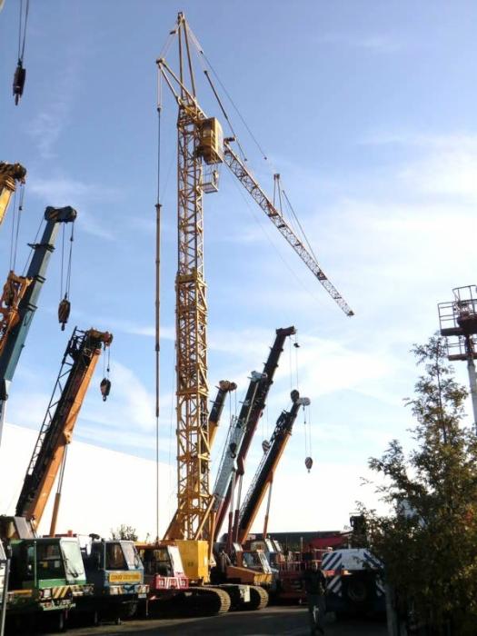 Żółty dźwig samojezdny Peiner CRL42-80 na placu budowy, otoczony innymi dźwigami i maszynami budowlanymi pod błękitnym niebem.