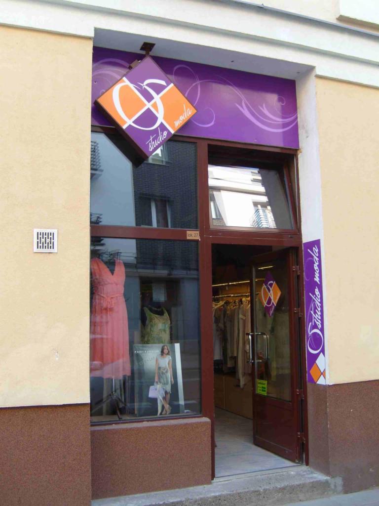 Wejście do sklepu odzieżowego Studio Moda z wystawą, na której widoczna jest sukienka na manekinie i plakat reklamowy.