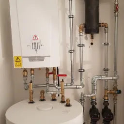 Nowoczesna kotłownia z białym kotłem De Dietrich, zasobnikiem Kospel i rozbudowaną instalacją hydrauliczną z rurami, zaworami i pompami obiegowymi