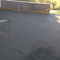 Usługi remontowo budowlane - Świeżo wylana, szara wylewka na tarasie z widoczną zacieraczką mechaniczną i zabezpieczeniami krawędzi.