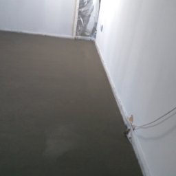 Usługi remontowo budowlane - Świeżo wylana, gładka wylewka anhydrytowa w jasnym pomieszczeniu, widoczne kable wystające ze ściany.