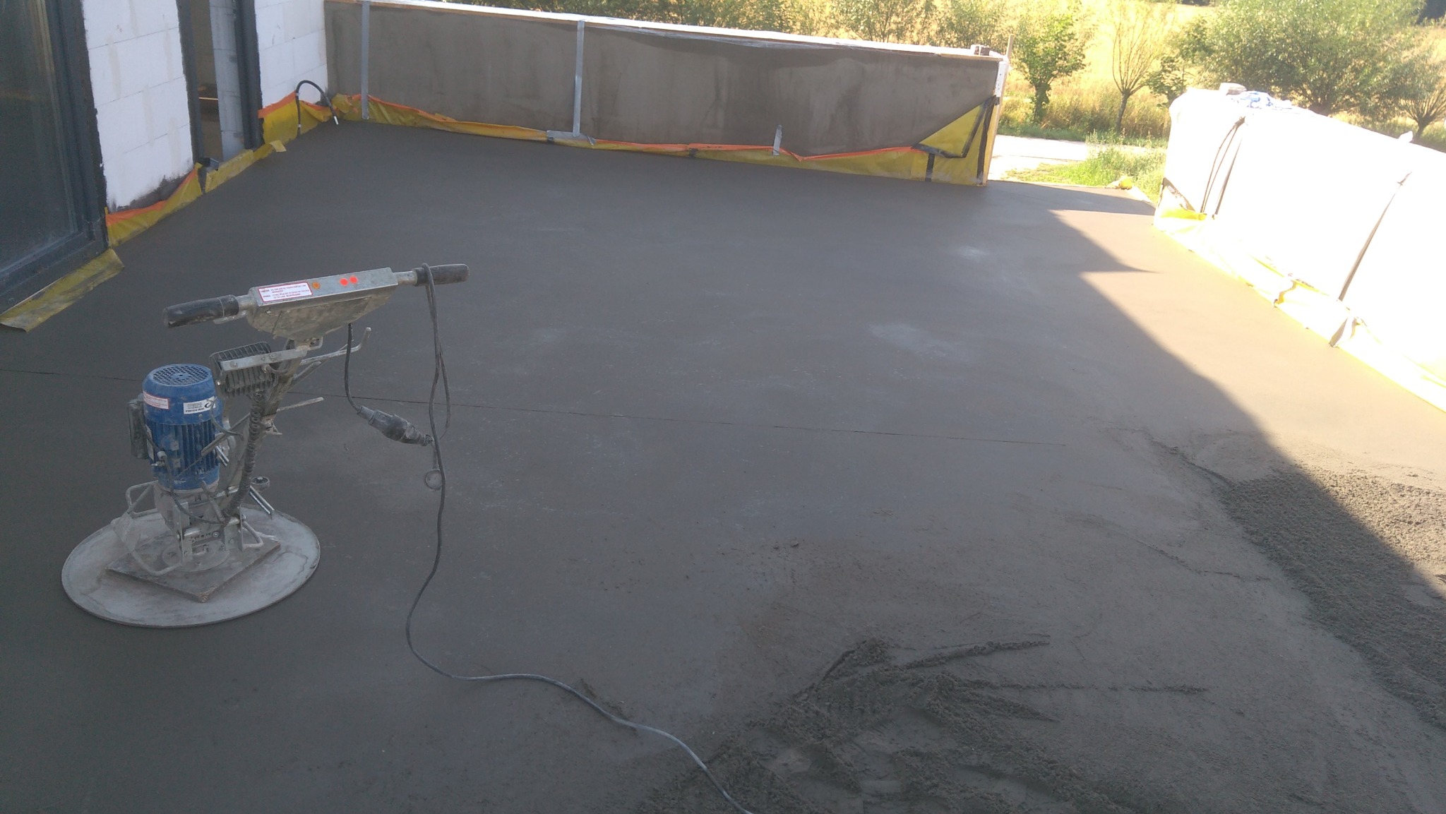 Świeżo wylana, szara wylewka na tarasie z widoczną zacieraczką mechaniczną i zabezpieczeniami krawędzi.