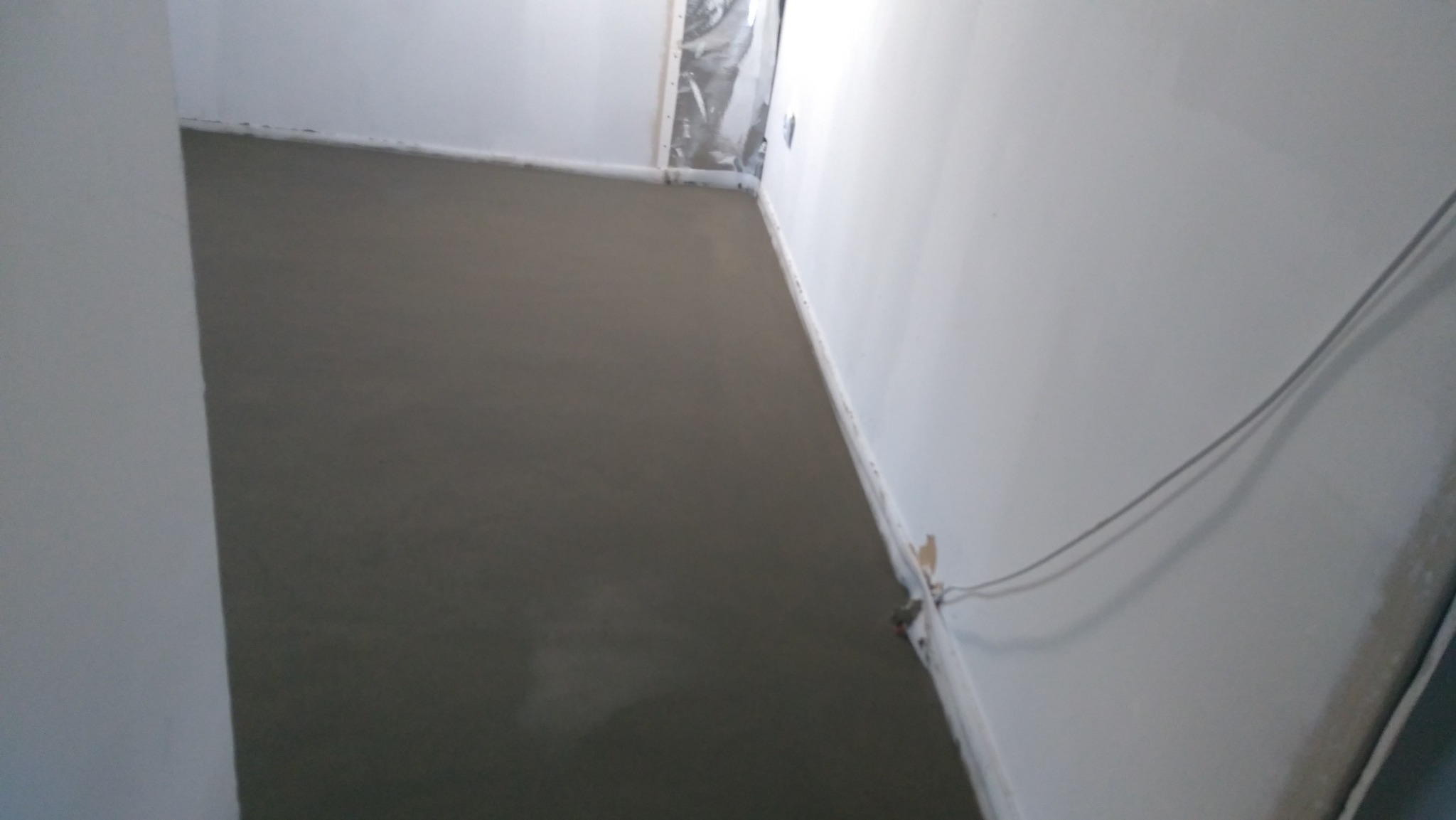 Świeżo wylana, gładka wylewka anhydrytowa w jasnym pomieszczeniu, widoczne kable wystające ze ściany.