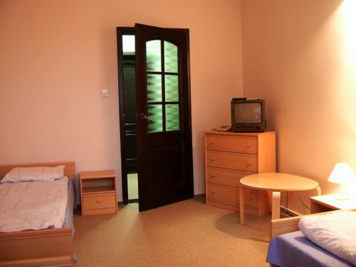 Pokój w ośrodku wypoczynkowym z dwoma pojedynczymi łóżkami, drewnianą komodą z telewizorem i stolikiem nocnym z lampką, drzwi balkonowe otwarte na zewnątrz.