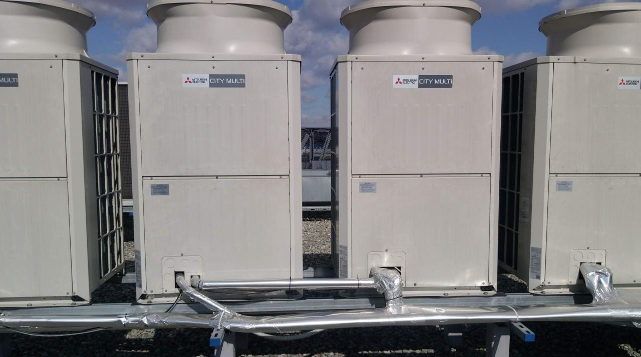 Cztery jednostki zewnętrzne klimatyzacji Mitsubishi Electric City Multi zamontowane na dachu budynku, z widocznymi rurami i izolacją.