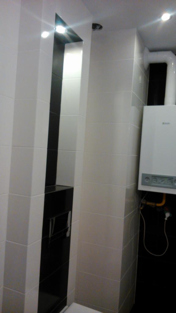 Nowoczesna łazienka z czarno-białymi płytkami, podświetlaną wnęką i wiszącym piecem gazowym Beretta z widoczną instalacją.