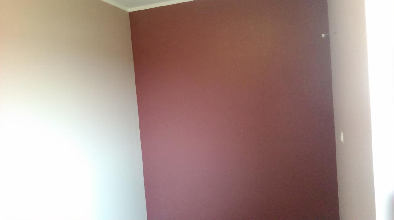 Pomieszczenie po malowaniu: ściana w kolorze bordowym sąsiaduje z kremową ścianą, widoczny narożnik i listwa przypodłogowa.