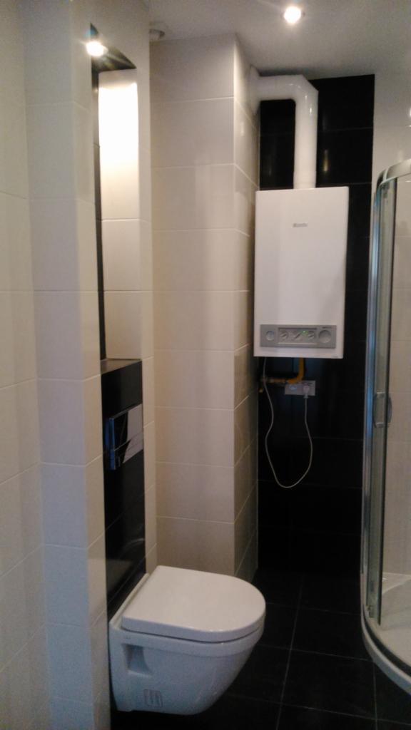 Nowoczesna łazienka z podwieszaną toaletą, czarno-białymi płytkami i wiszącym piecem gazowym z białym kominem.