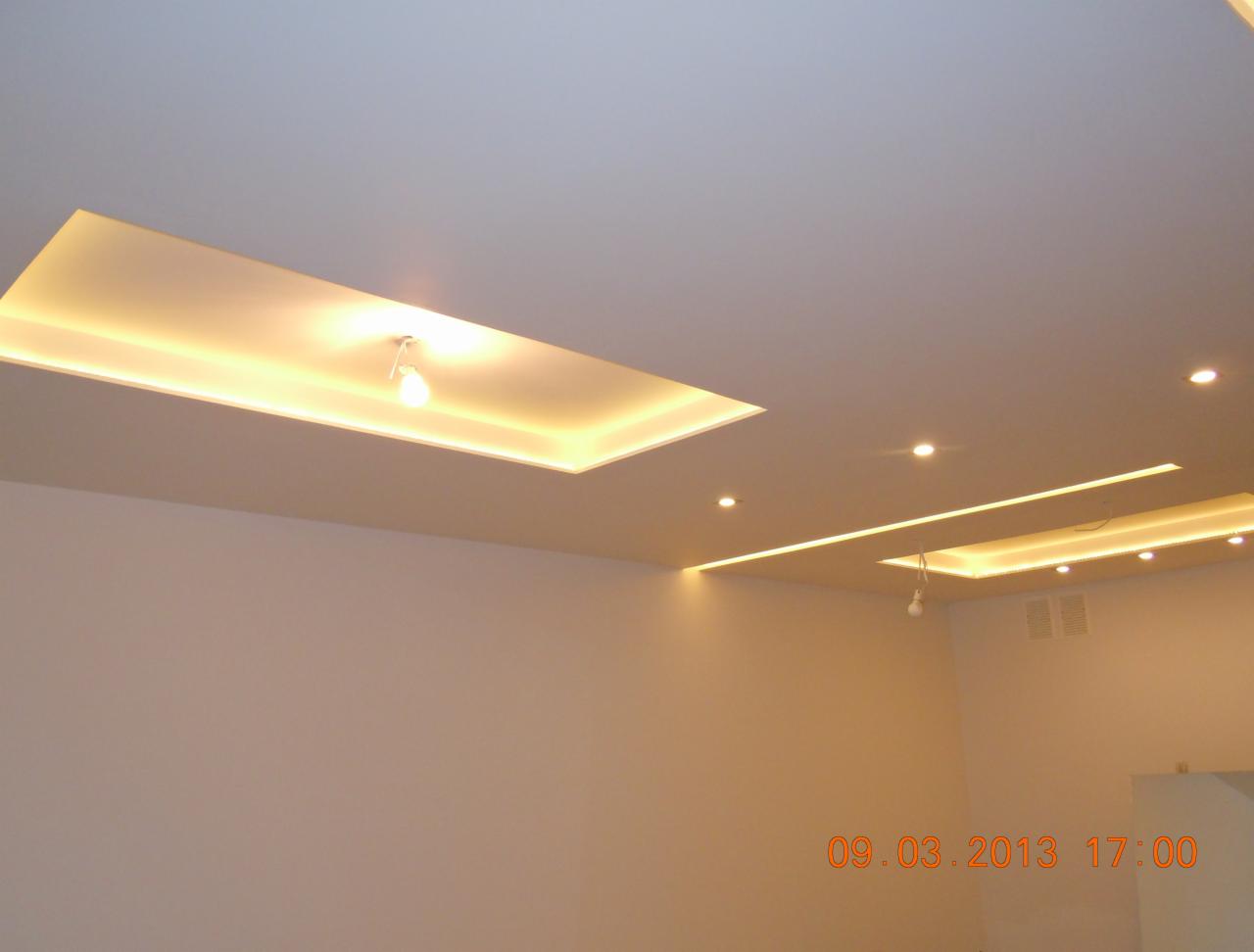 Nowoczesny sufit podwieszany z oświetleniem LED w kształcie prostokątów i punktowych reflektorów, pomalowany na jasny kolor, widok z dołu.