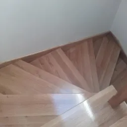 Kątowe ujęcie z góry na jasne, lakierowane stopnie w Wieliczce, tworzące zakręt schodów przy białej ścianie.