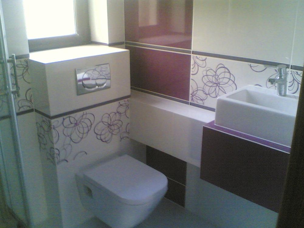 Wykończona łazienka z białymi i bordowymi płytkami, dekoracyjnym motywem kwiatowym, podwieszaną toaletą i prostokątną umywalką.