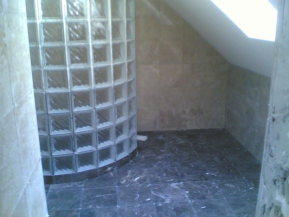 Wykończona łazienka w trakcie remontu, z kabiną prysznicową z luksferów, ciemną marmurową podłogą i płytkami imitującymi kamień na ścianach, widoczne niedociągnięcia w wykończeniu.