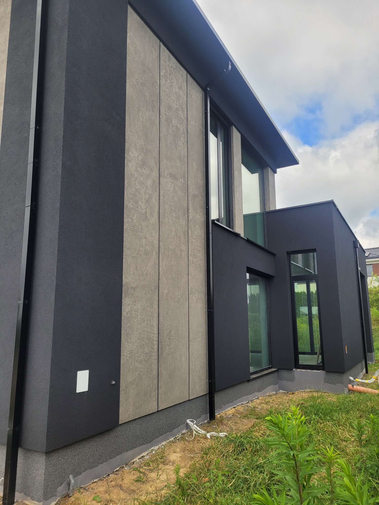 Nowoczesna elewacja domu z panelami w odcieniach szarości i czerni, widok z dołu, podkreślający geometrię budynku i minimalistyczny design.