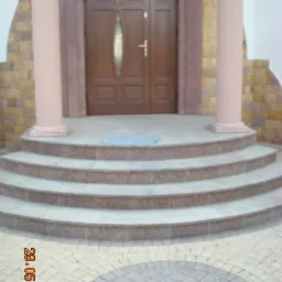 Wejście do domu z brązowymi drzwiami, kolumnami i czterostopniowymi schodami z jasnego kamienia, wykończone kostką brukową w dwóch odcieniach szarości.