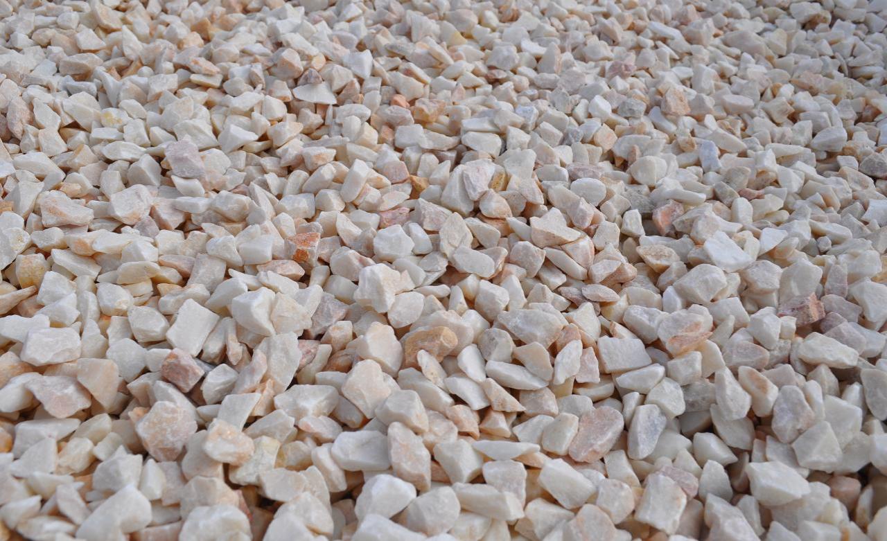 Biało-różowe kruszywo marmurowe o nieregularnych kształtach, tworzące gęstą teksturę, oświetlone naturalnym światłem.