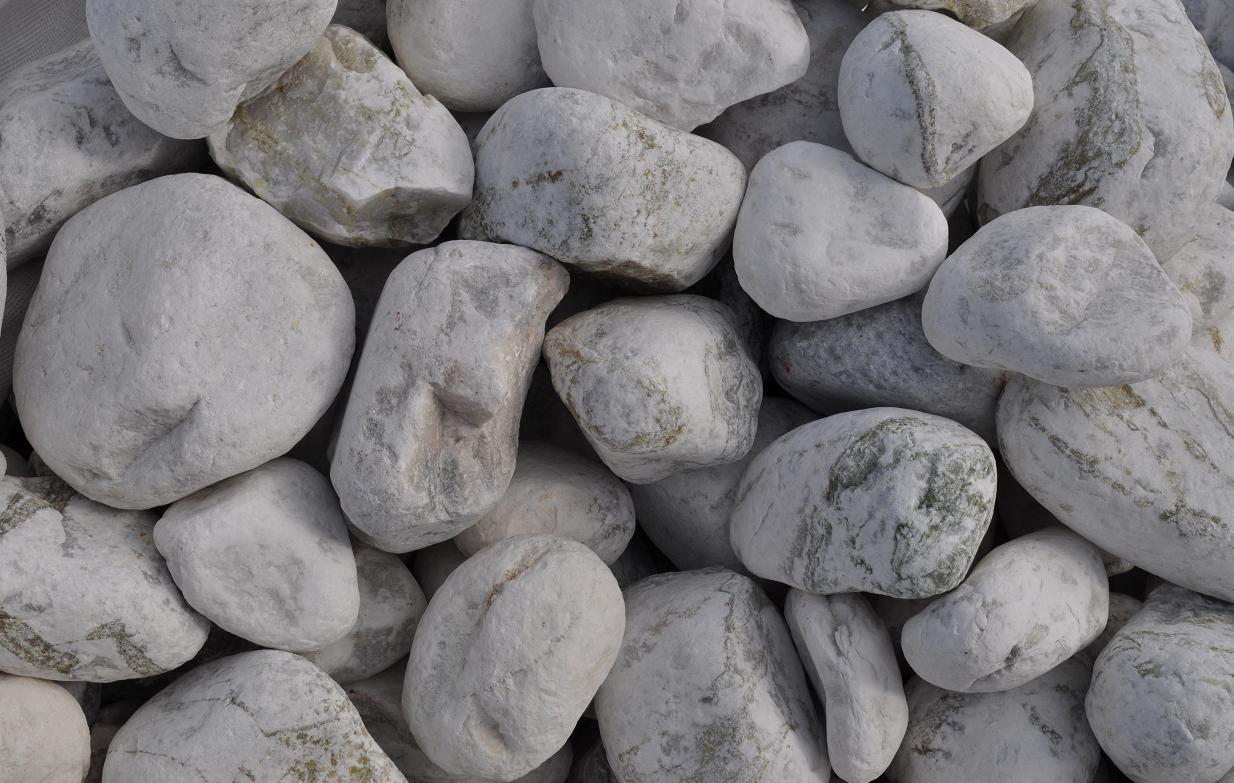 Stos białych, otoczaków rzecznych o zróżnicowanej fakturze i odcieniach szarości, przeznaczonych do dekoracji ogrodów lub jako element wykończeniowy.