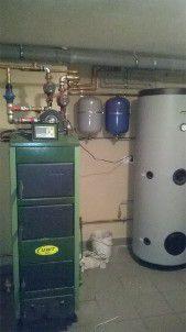 Zielony piec CO z podłączonymi rurami miedzianymi, dwa zbiorniki wyrównawcze i duży, szary zasobnik ciepłej wody w kotłowni.