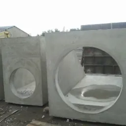 Betonowe prefabrykaty z okrągłymi otworami, prawdopodobnie elementy kanalizacji deszczowej, ustawione na placu budowy.