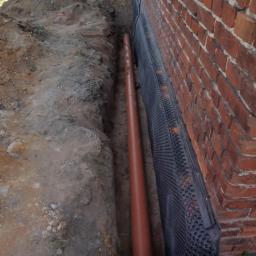 Ryszard Golenia - Wykonanie izolacji pionowej fundamentu z użyciem membrany kubełkowej oraz rury drenarskiej w wykopie przy ceglanej ścianie budynku.